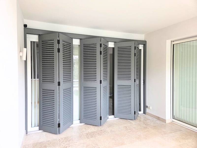 Volets persiennes pliants accordéon à lames à la française installés sur une grande baie vitrée d’une villa près d’Antibes. 